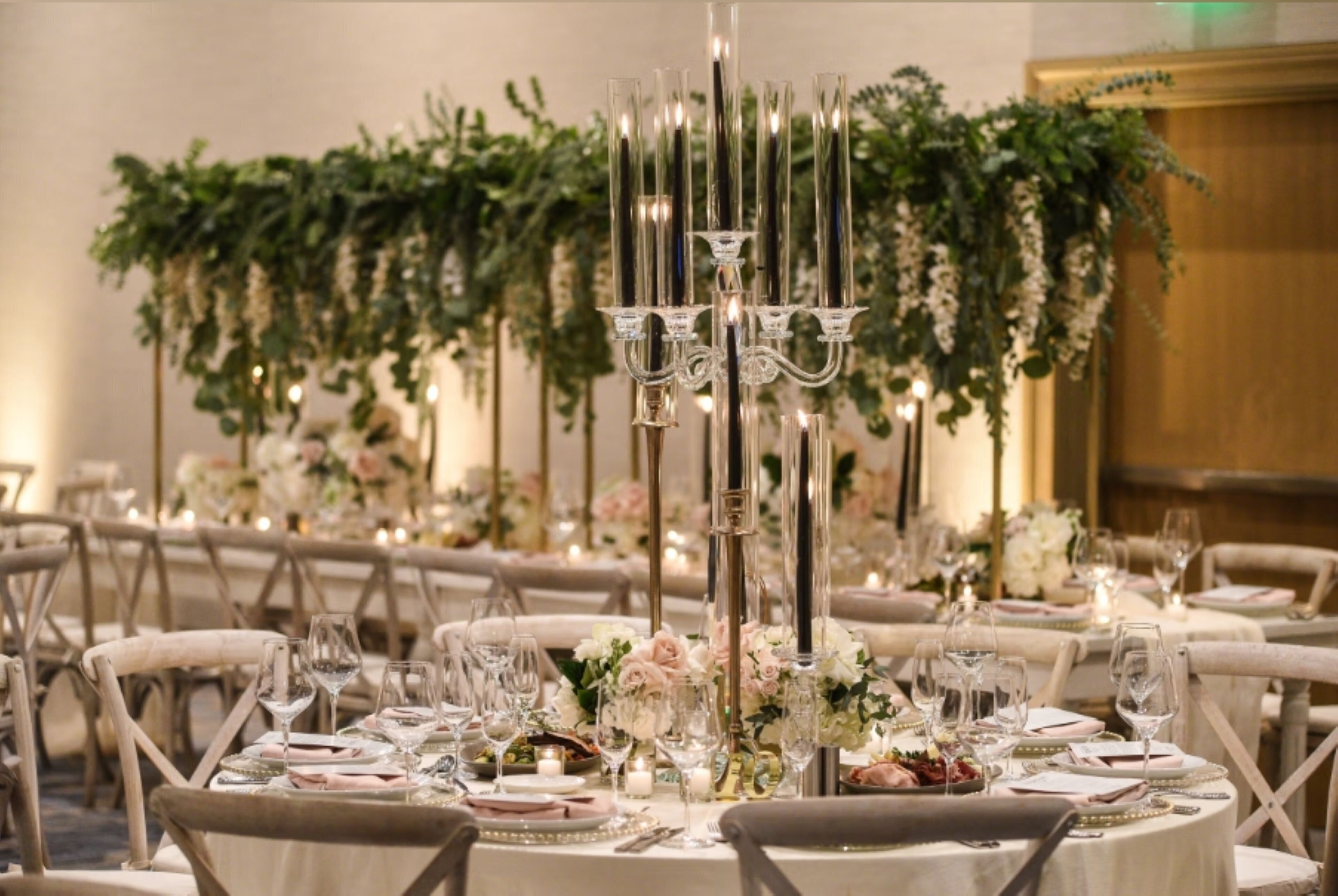 A banquet hall with round tables set for a formal event, featuring floral centerpieces and candle holders.