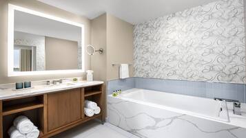 A modern bathroom with a large mirror, marble bathtub, wooden vanity, and patterned wallpaper.