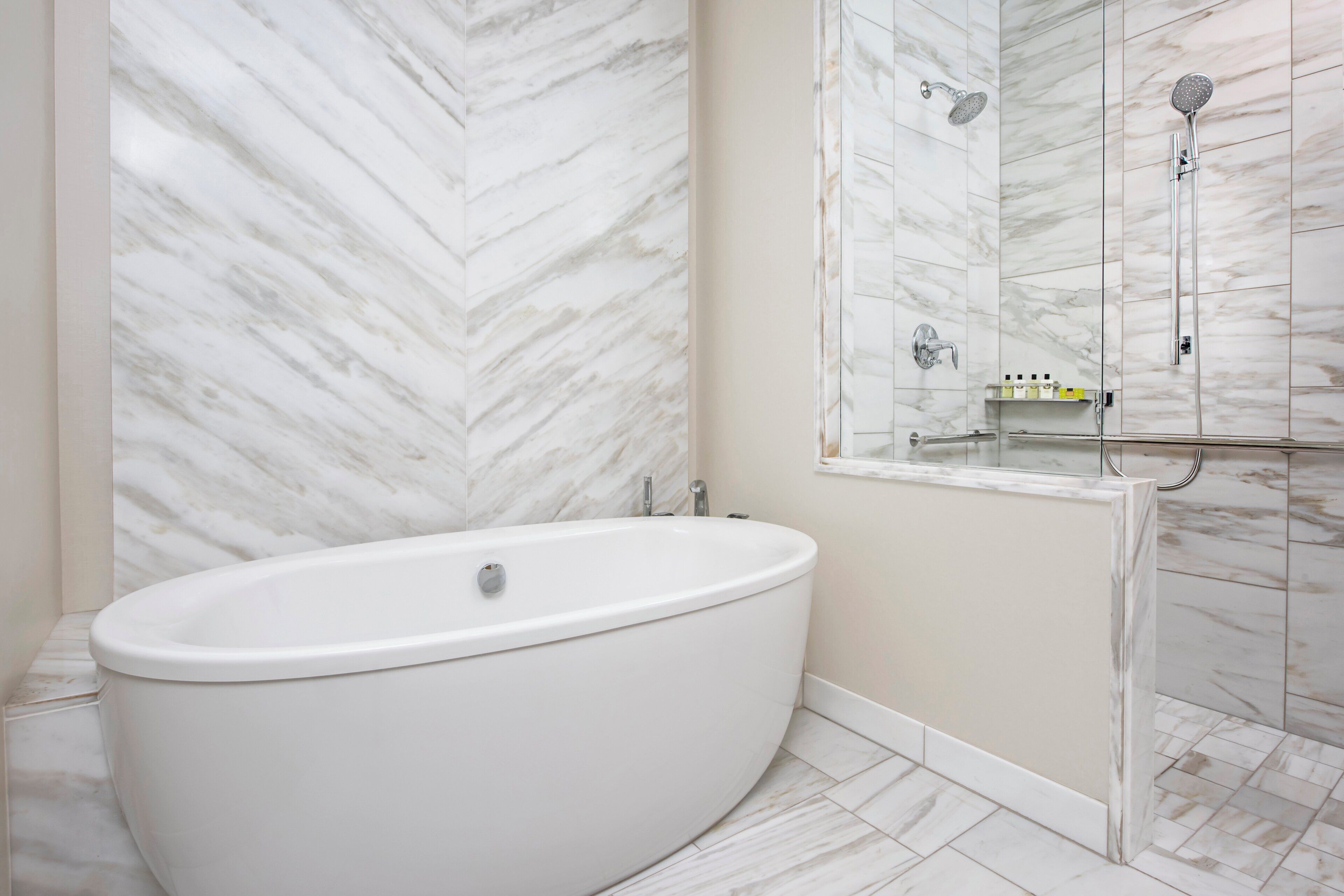 A modern bathroom with a freestanding bathtub, a shower enclosure, and a marble-patterned wall.