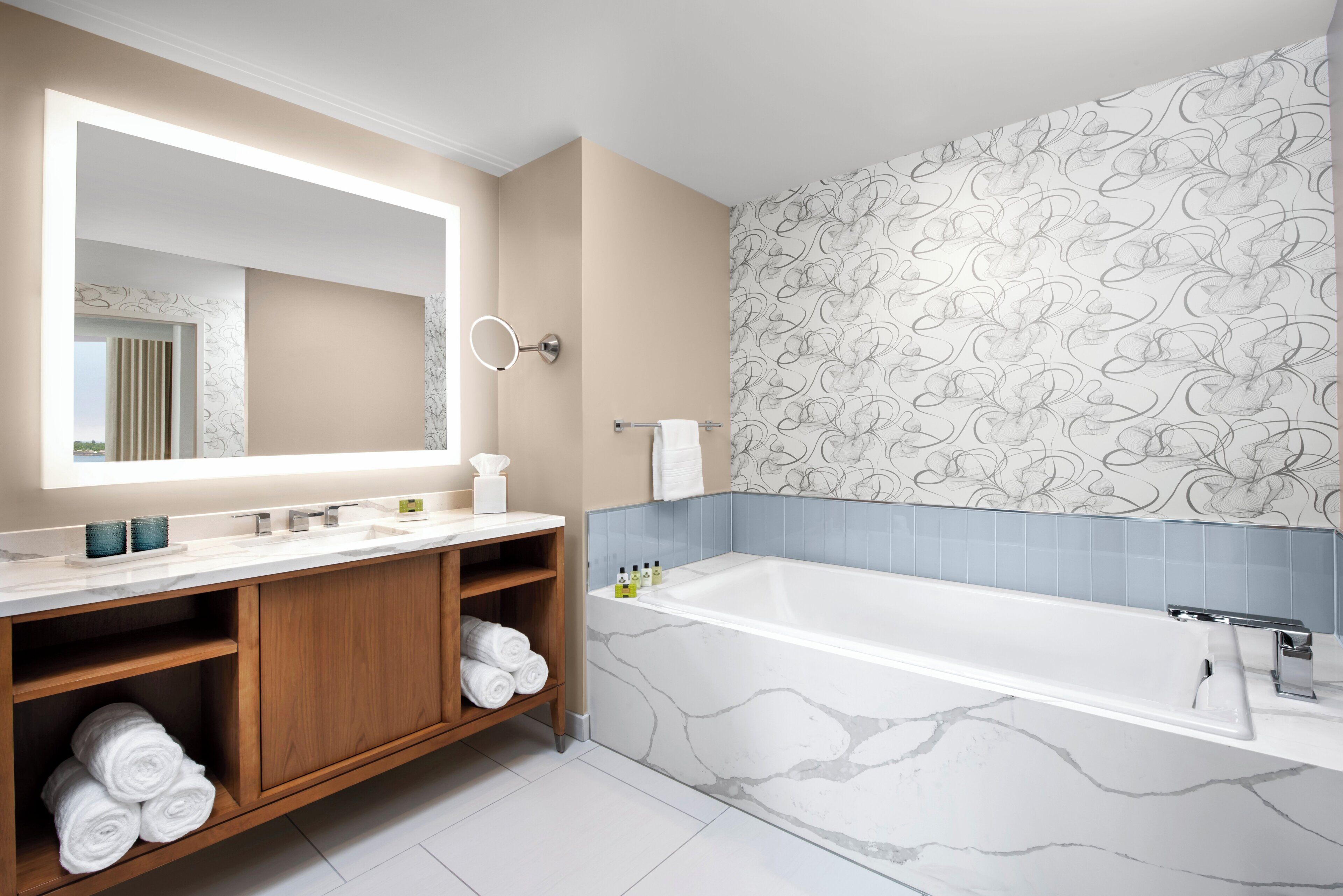 Une salle de bain moderne avec un grand miroir, une baignoire et un meuble-lavabo avec des serviettes.