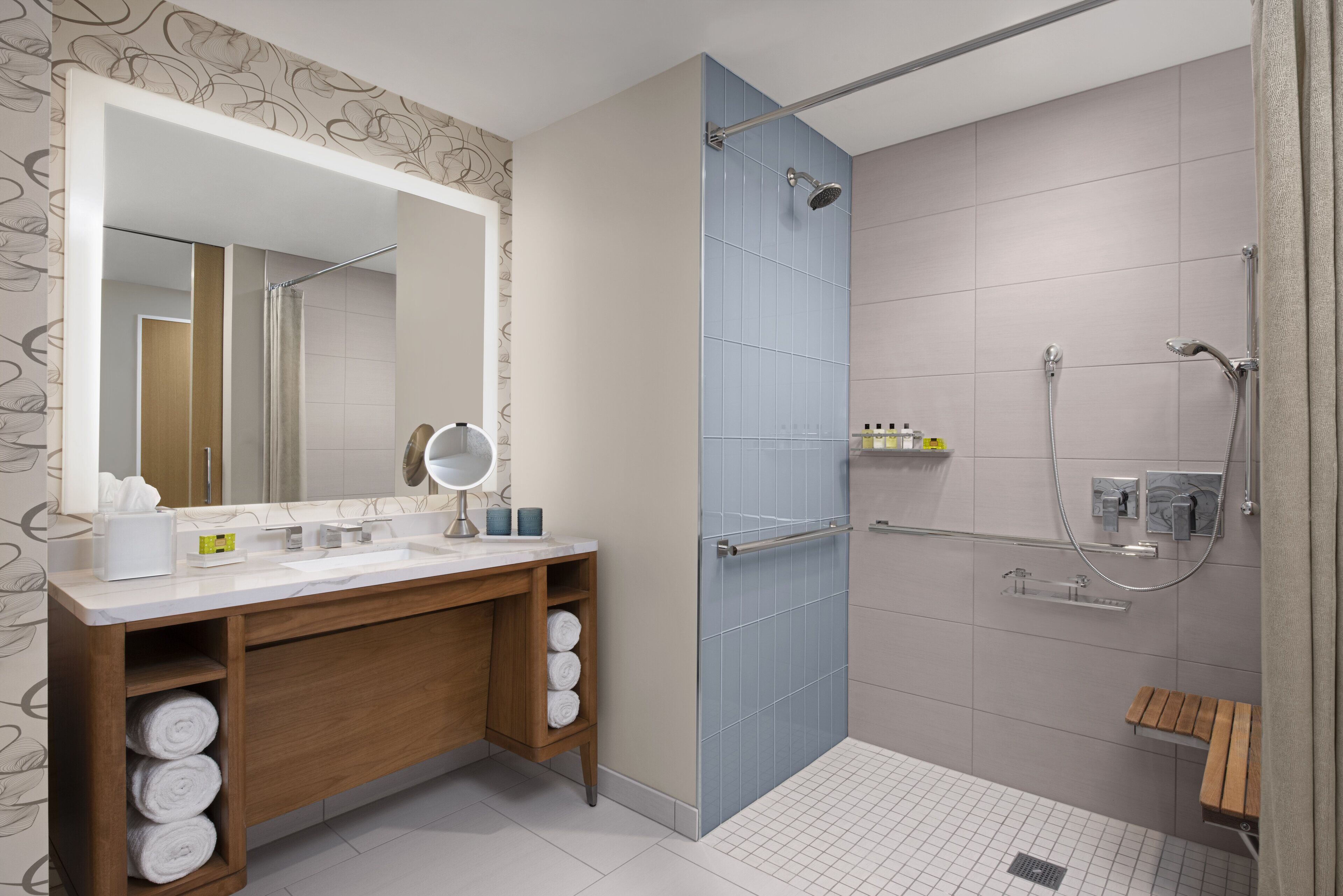 A modern bathroom with a wooden vanity, a large mirror, a shower with a glass door, and a tiled floor.