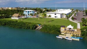 A coastal property with a large white building, a blue house, and a thatched-roof structure. There are boats docked near the water. - Hampton Inn Marathon - Florida Keys (Marathon)
