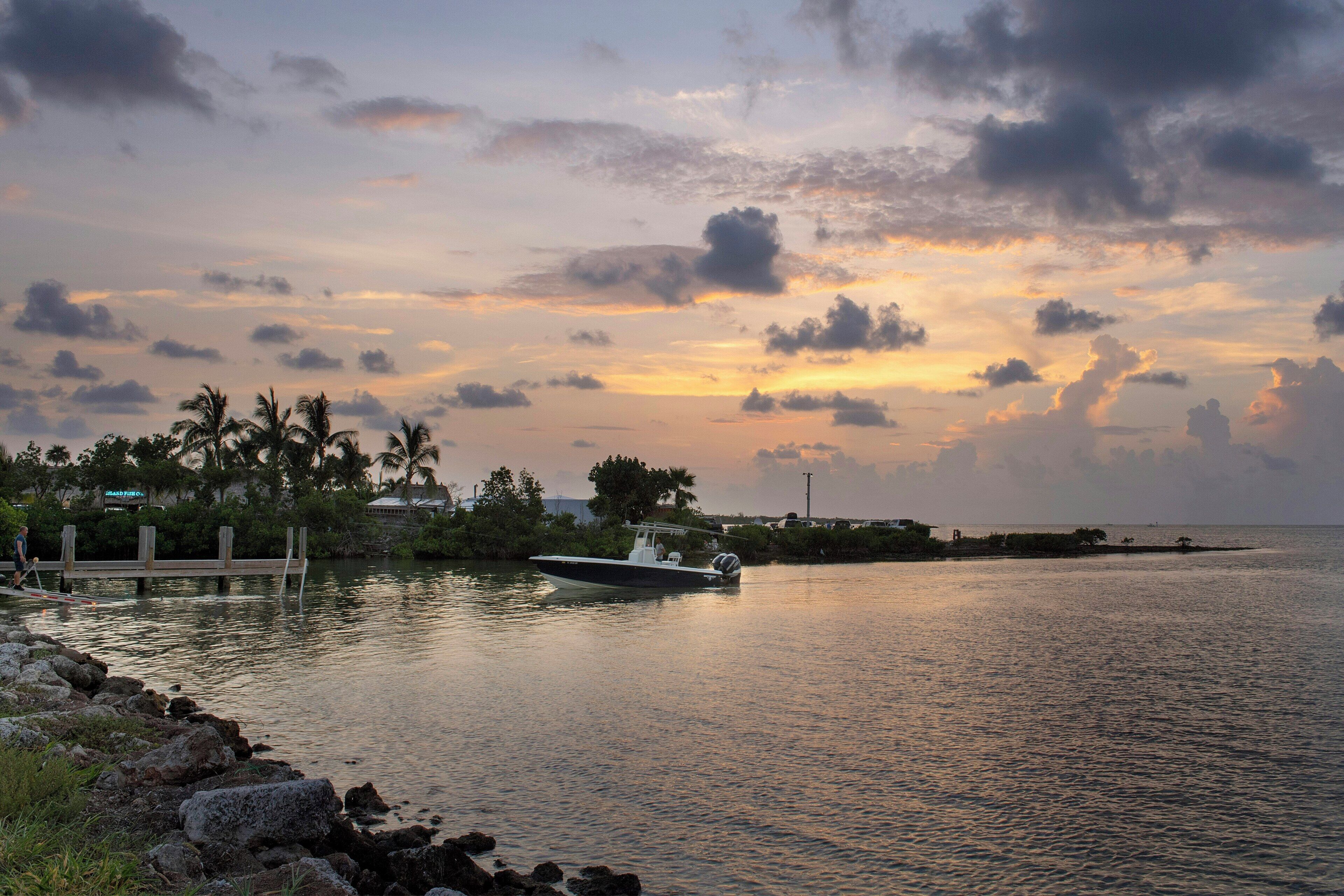 A calm body of water with a boat, a dock, and a distant shoreline with vegetation and buildings.