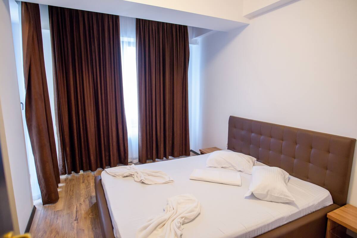 Una habitación de hotel con una cama grande, cortinas marrones y suelo de madera.