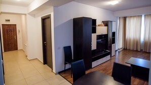A modern living room with a wooden floor, a black sofa, a dining table, and a TV stand. - Beach Vibe Apartments  Summerland Mamaia (Constanta)