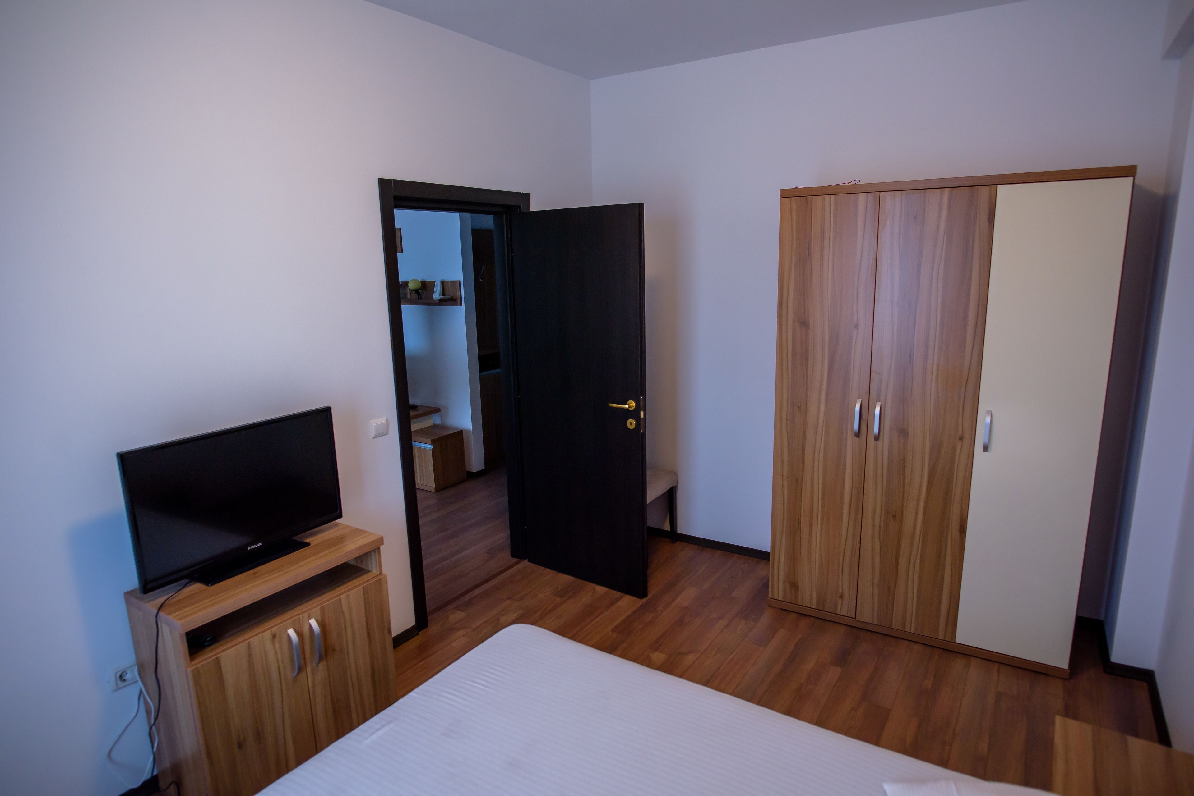 A room with a bed, a TV on a wooden stand, a wardrobe, and a door leading to another room.