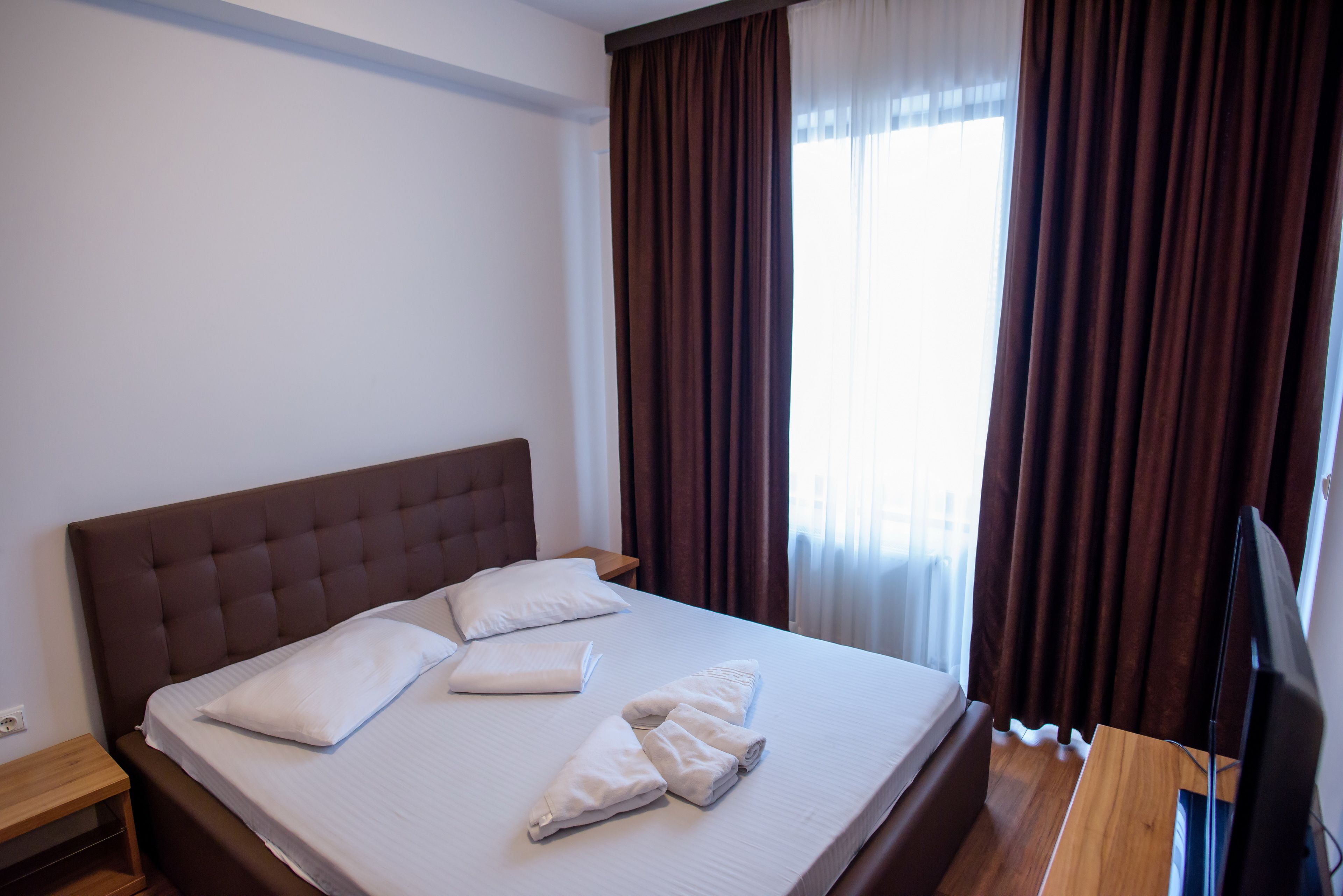 A neatly made bed with pillows and towels, a wooden nightstand, and a television on a wooden stand.
