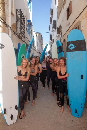 A group of people holding surfboards in a narrow street.