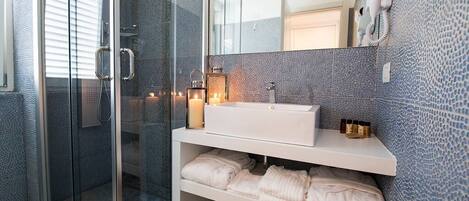 Un baño moderno con cabina de ducha de vidrio, tocador blanco con espejo y pared azul con textura.