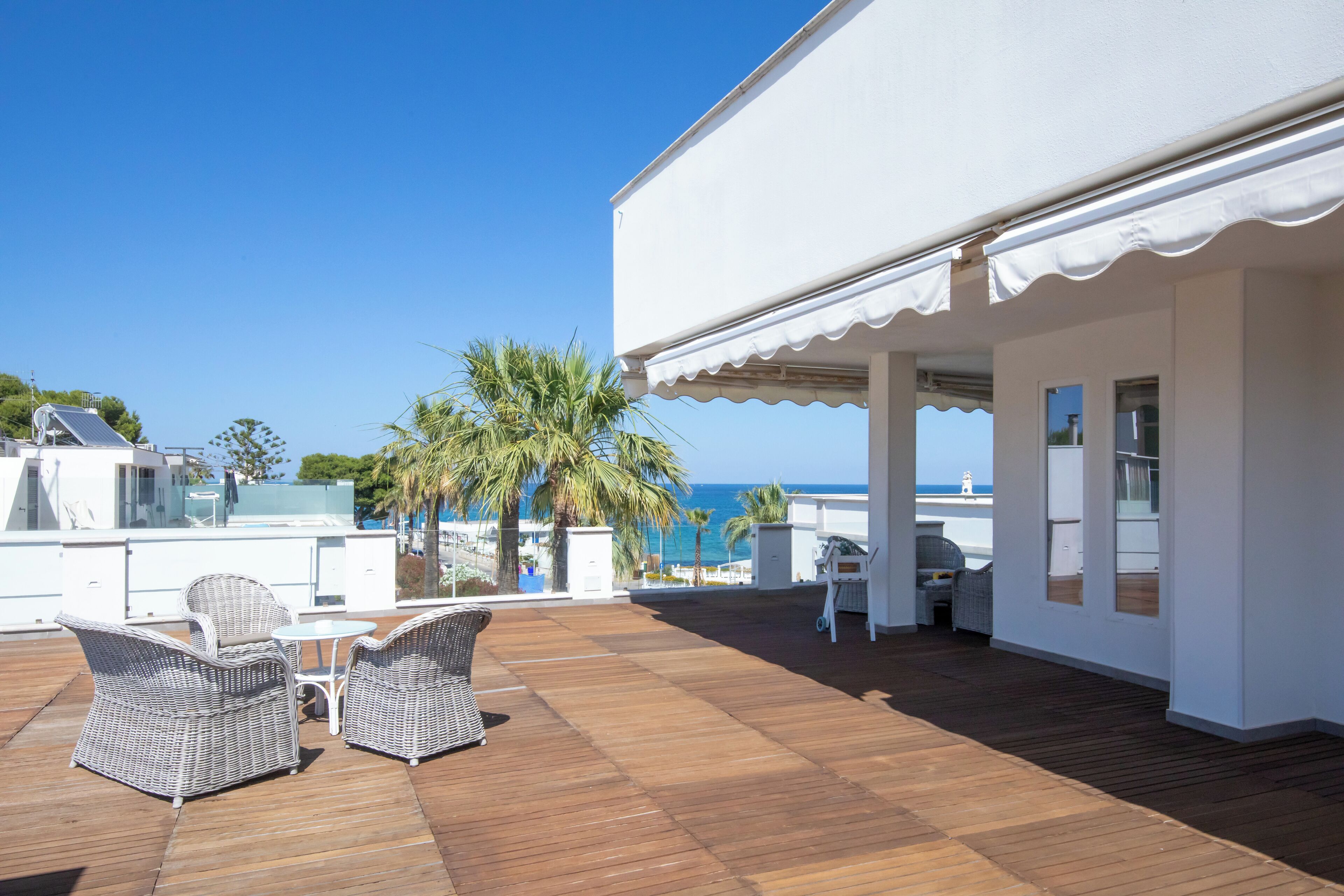 Un patio techado al aire libre con mobiliario de mimbre, una terraza de madera y vistas al mar.