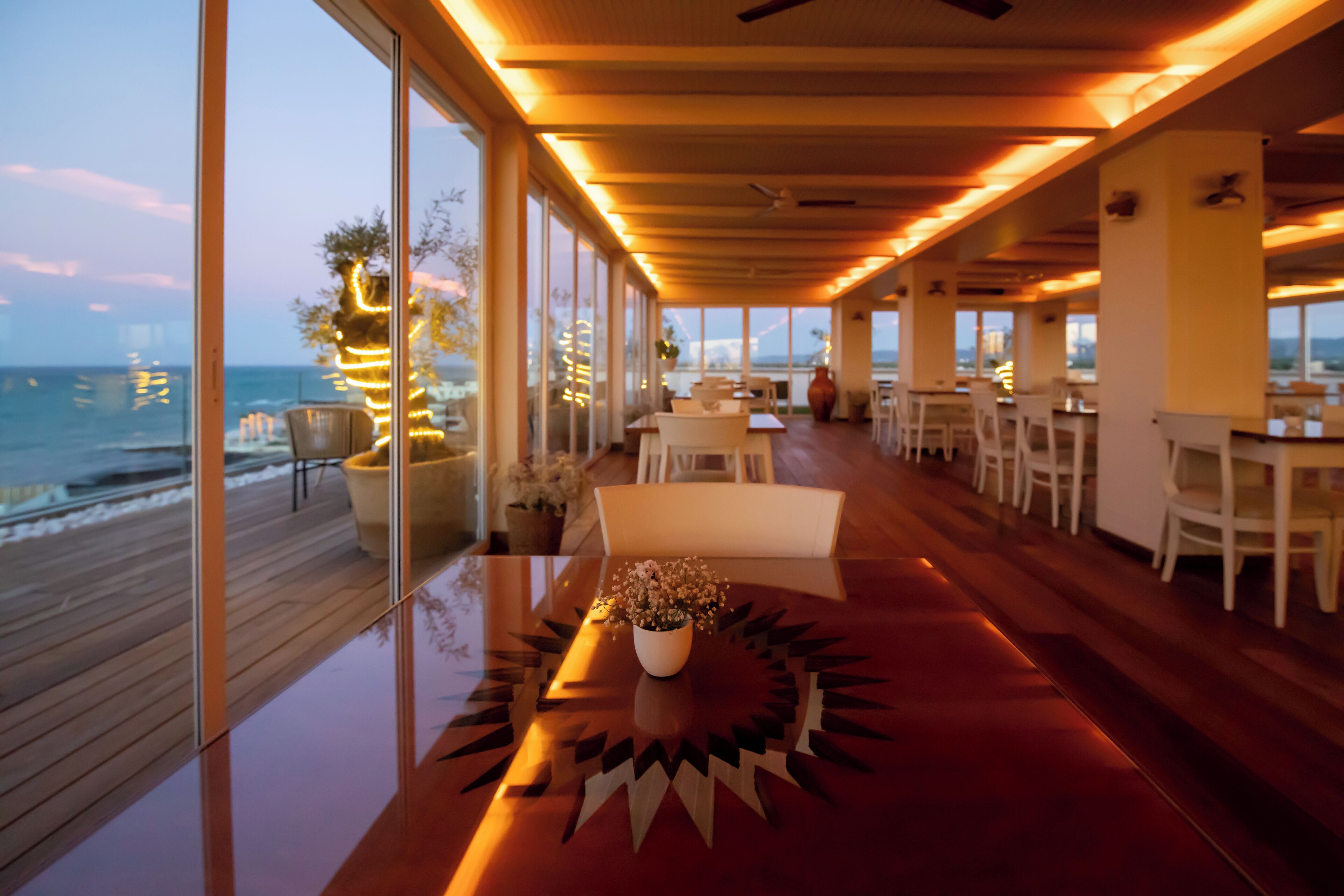 Un intérieur moderne avec un grand espace de salle à manger, de grandes fenêtres donnant sur la mer et une table centrale agrémentée d’un vase de fleurs.