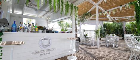A pool bar area with white furniture, hanging plants, and a wooden ceiling.