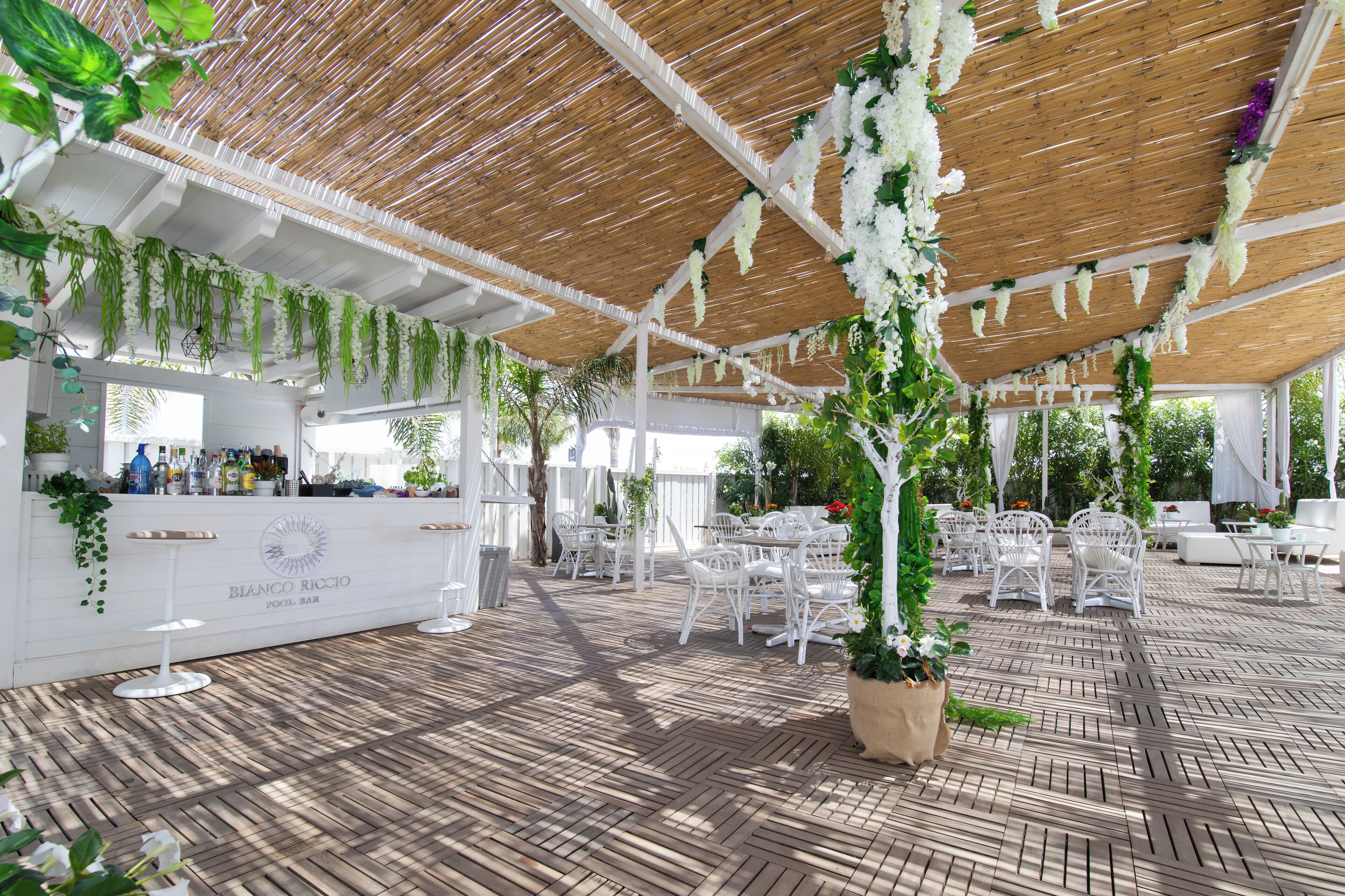 An outdoor patio area with white furniture, a bar counter, and hanging plants.