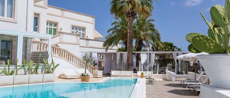 A pool area with a clear blue pool, white lounge chairs, and palm trees.