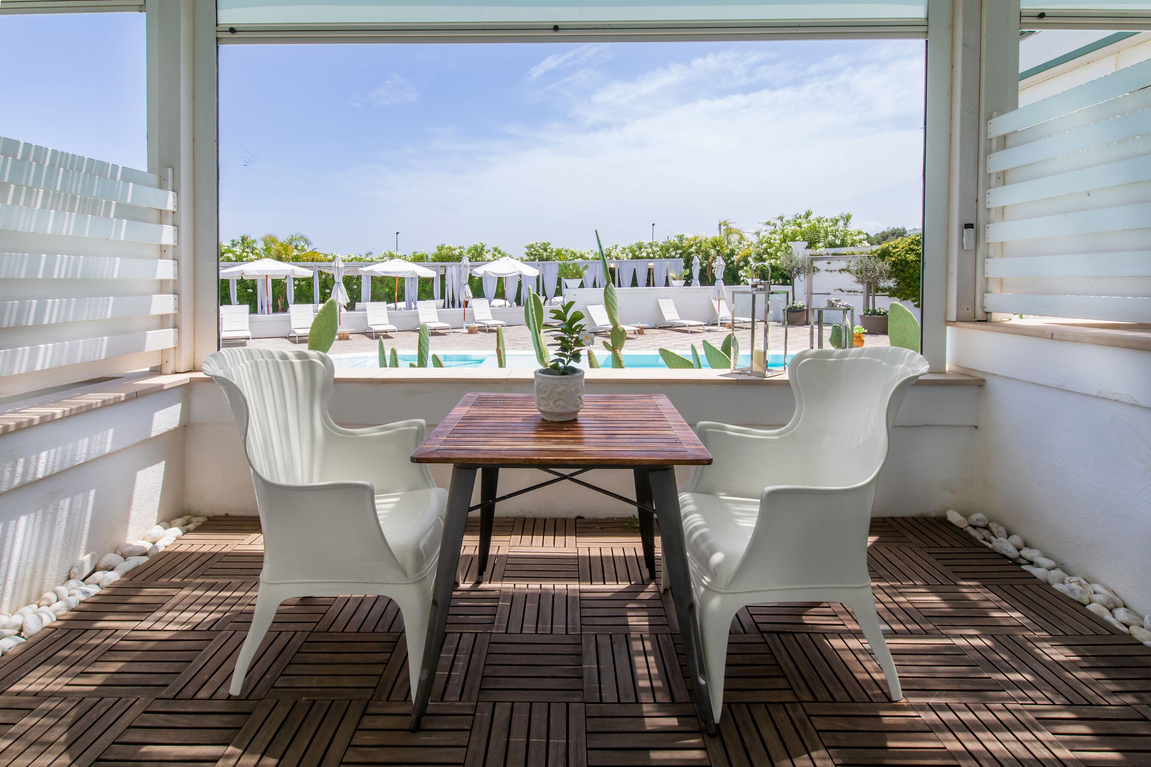 Eine Terrasse mit Tisch und Stühlen, mit Blick auf einen Poolbereich mit Sonnenschirmen und Liegestühlen.