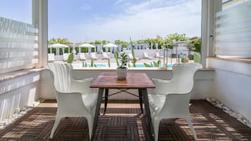 Eine Terrasse mit Tisch und Stühlen, mit Blick auf einen Poolbereich mit Sonnenschirmen und Liegestühlen.