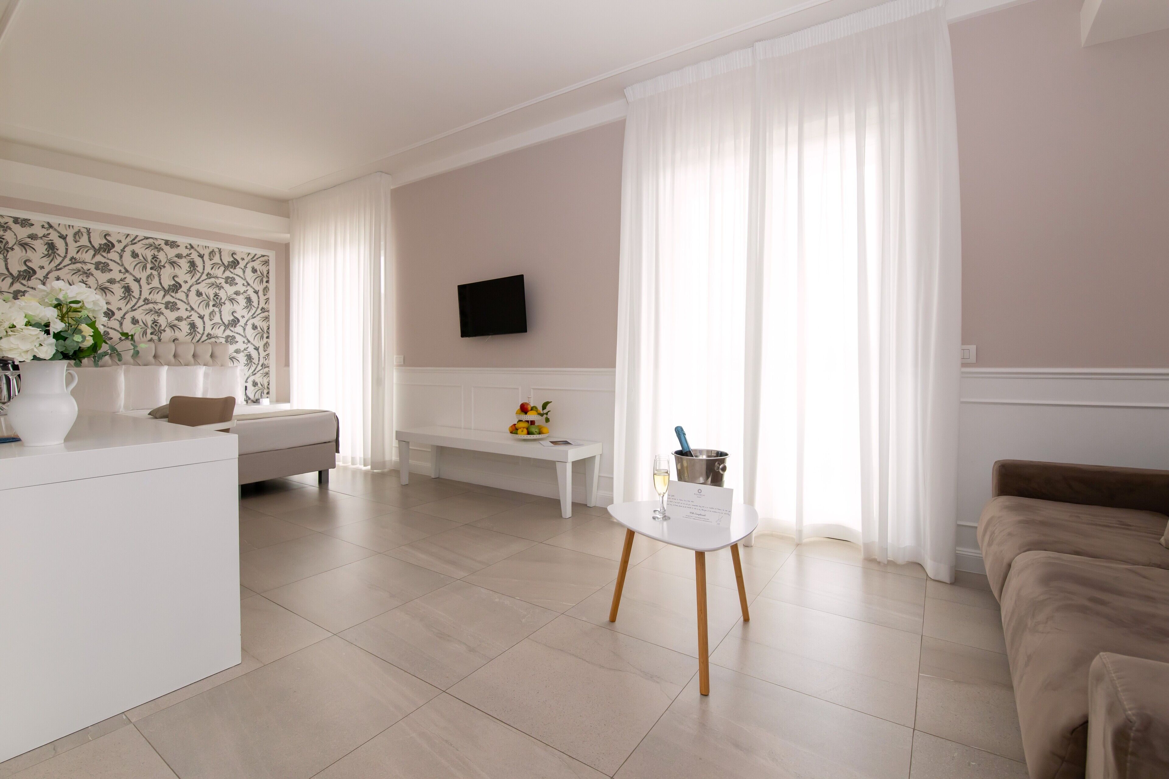 A modern living room with a white sofa, a beige sofa, a white coffee table, and a television mounted on the wall.