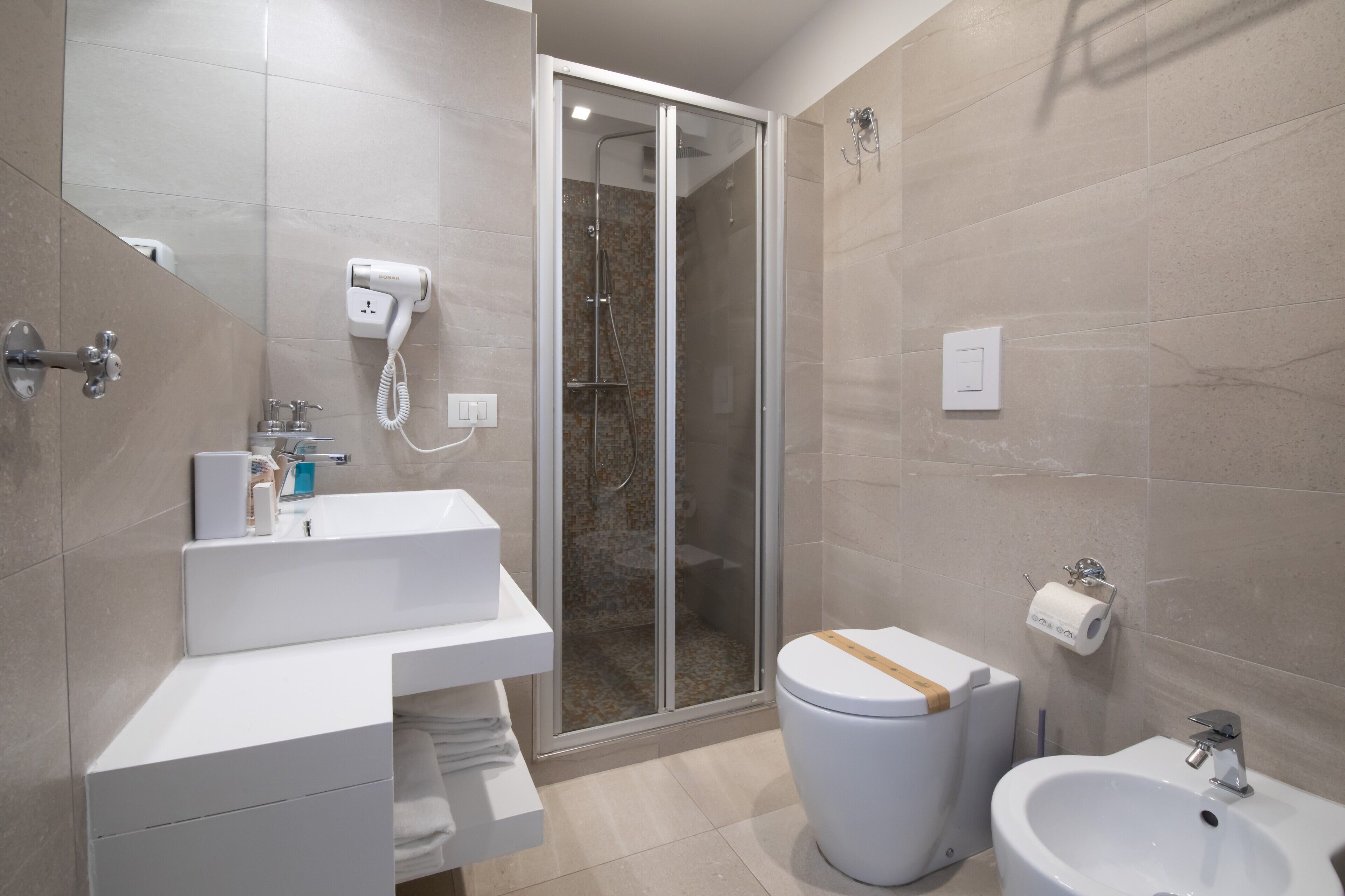 A modern bathroom with a shower, toilet, bidet, and a sink with a towel rack.