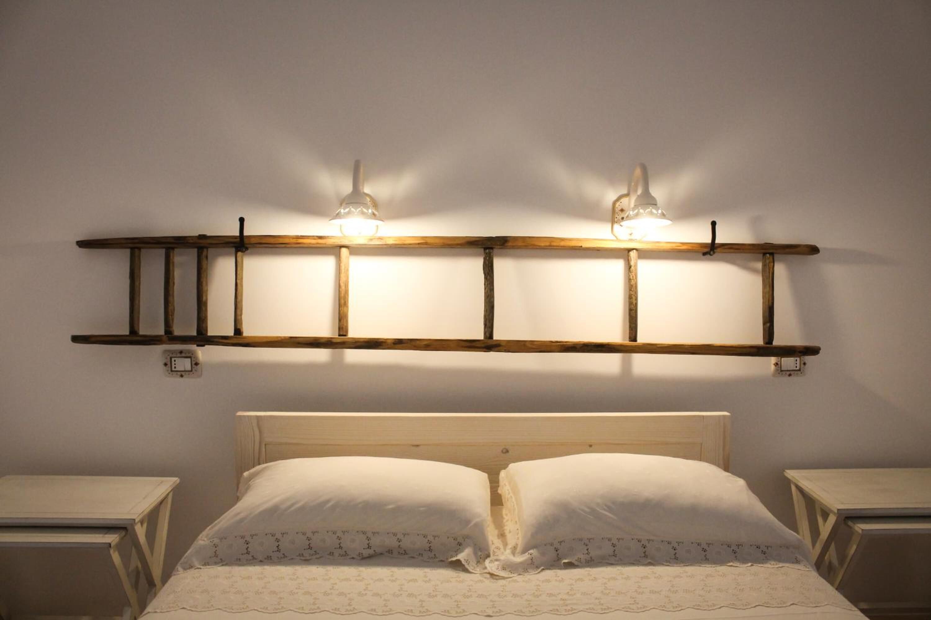 Una cama con cabecera de madera, dos mesitas de noche y una lámpara fijada a la pared.