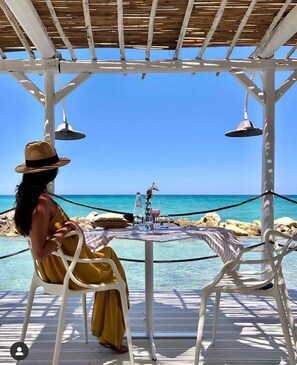 A person seated at a table with a view of the sea under a wooden pergola. - Tenuta Palmira (Salve)