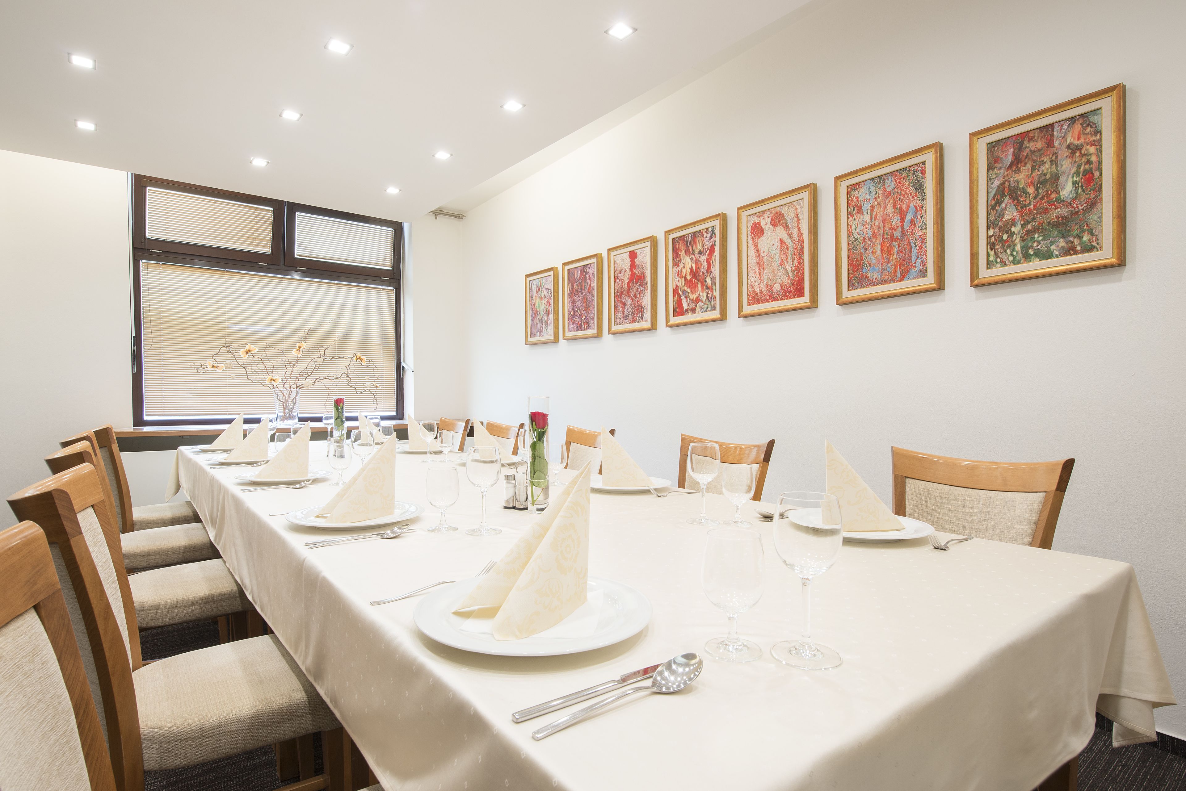 Comedor con una mesa larga dispuesta para una comida, sillas y cuadros en la pared.