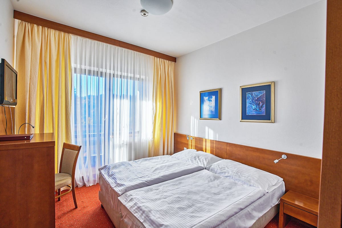Habitación de hotel con dos camas, un escritorio, una silla y dos cuadros en la pared.