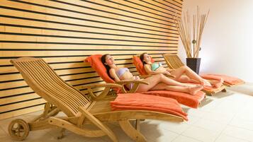 A room with wooden slat walls, wooden loungers with orange towels, and a potted plant.