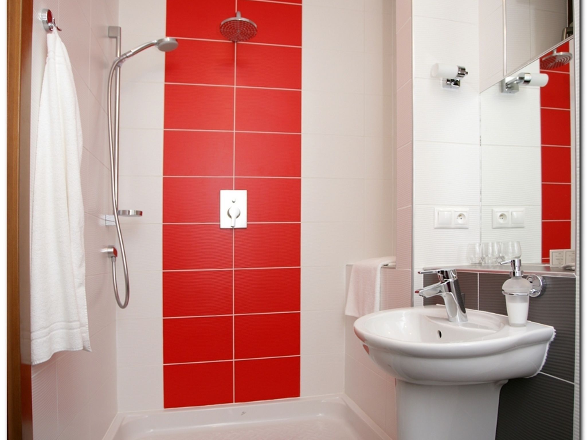 A bathroom with a red tiled shower wall, a white sink, and a mirror.
