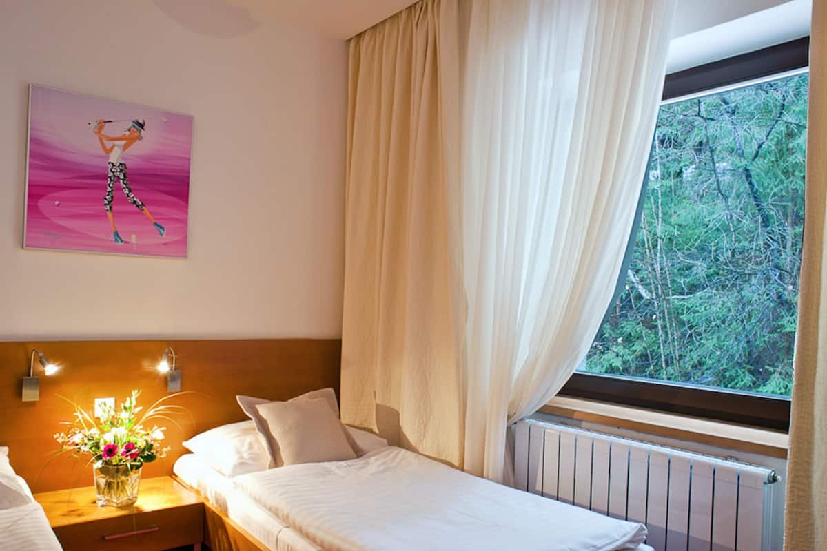Habitación de hotel con cama, mesita de noche con lámpara, un cuadro en la pared y ventana con cortinas.