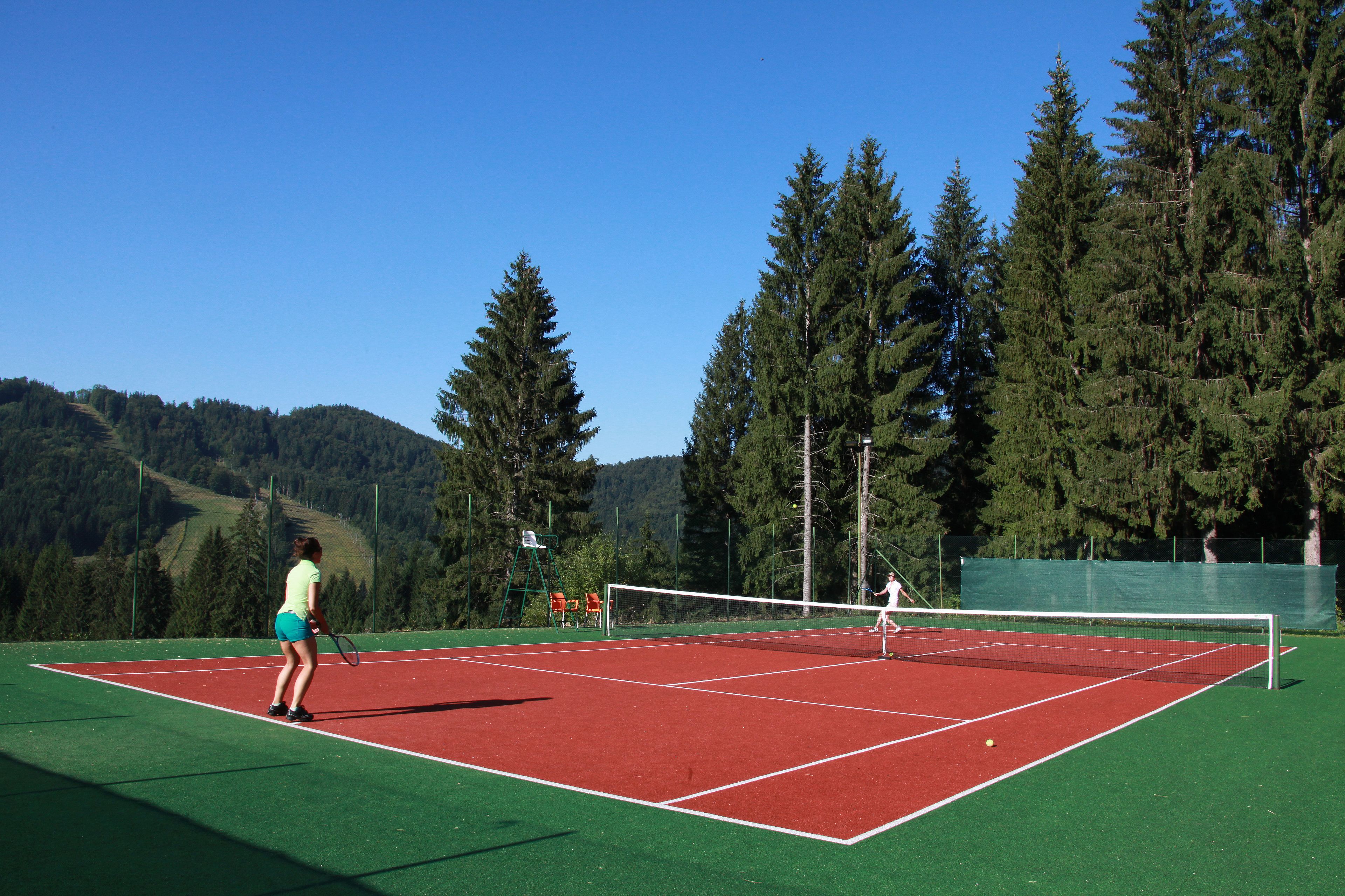 A tennis court with a net, surrounded by trees and a hilly landscape.