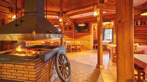 Een rustiek houten interieur met een metselwerk openhaard, houten tafels en een groot houten rad.