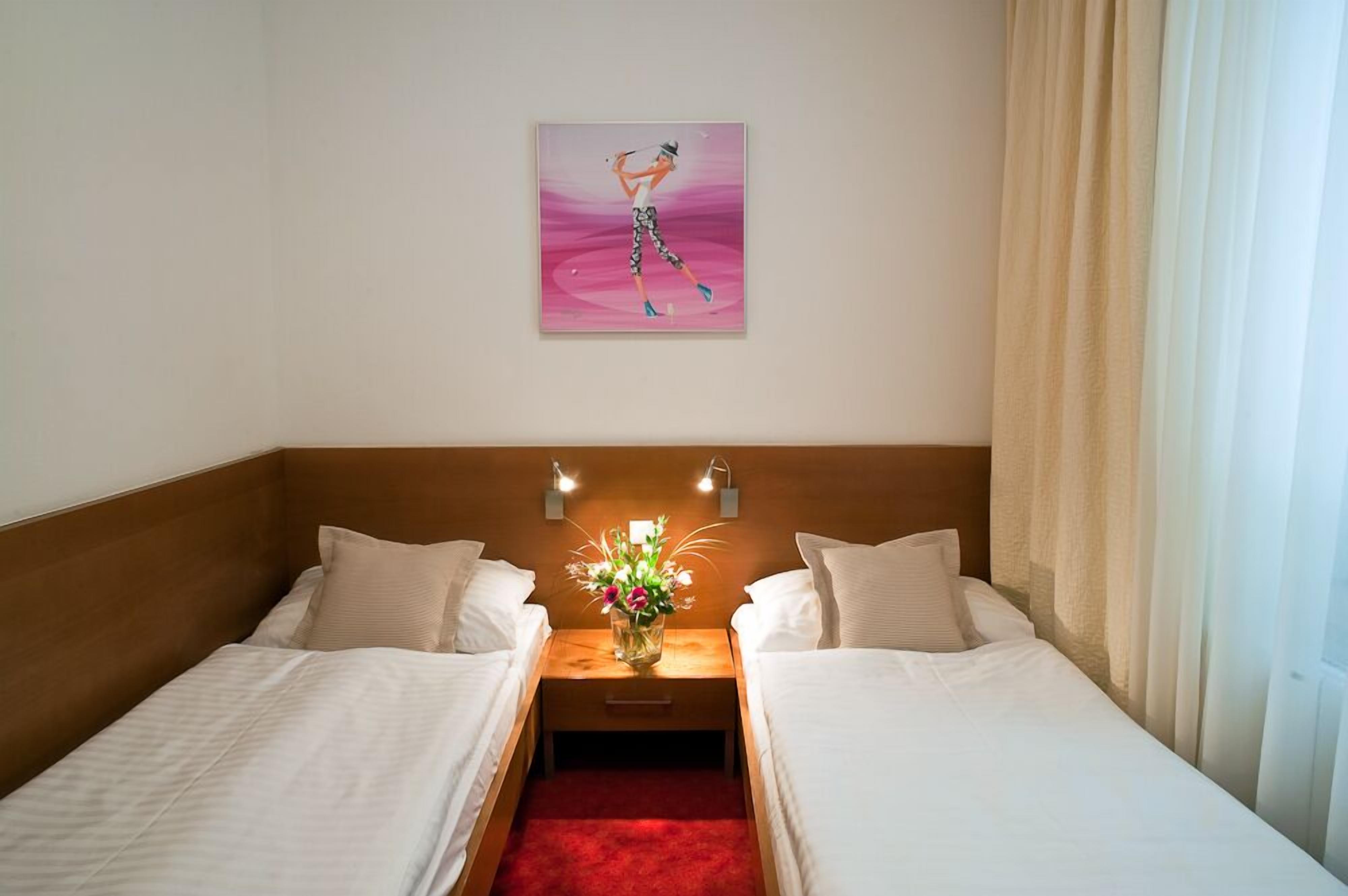A hotel room with two single beds, a nightstand with a vase of flowers, and a painting on the wall.