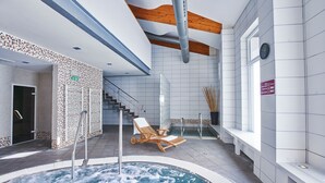 Een modern binnenzwembad met een jacuzzi, houten lounge fauteuils en een trap naar een hoger niveau.