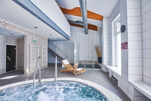 Uma piscina interior moderna com hidromassagem, espreguiçadeiras de madeira e uma escadaria que leva a um andar superior.