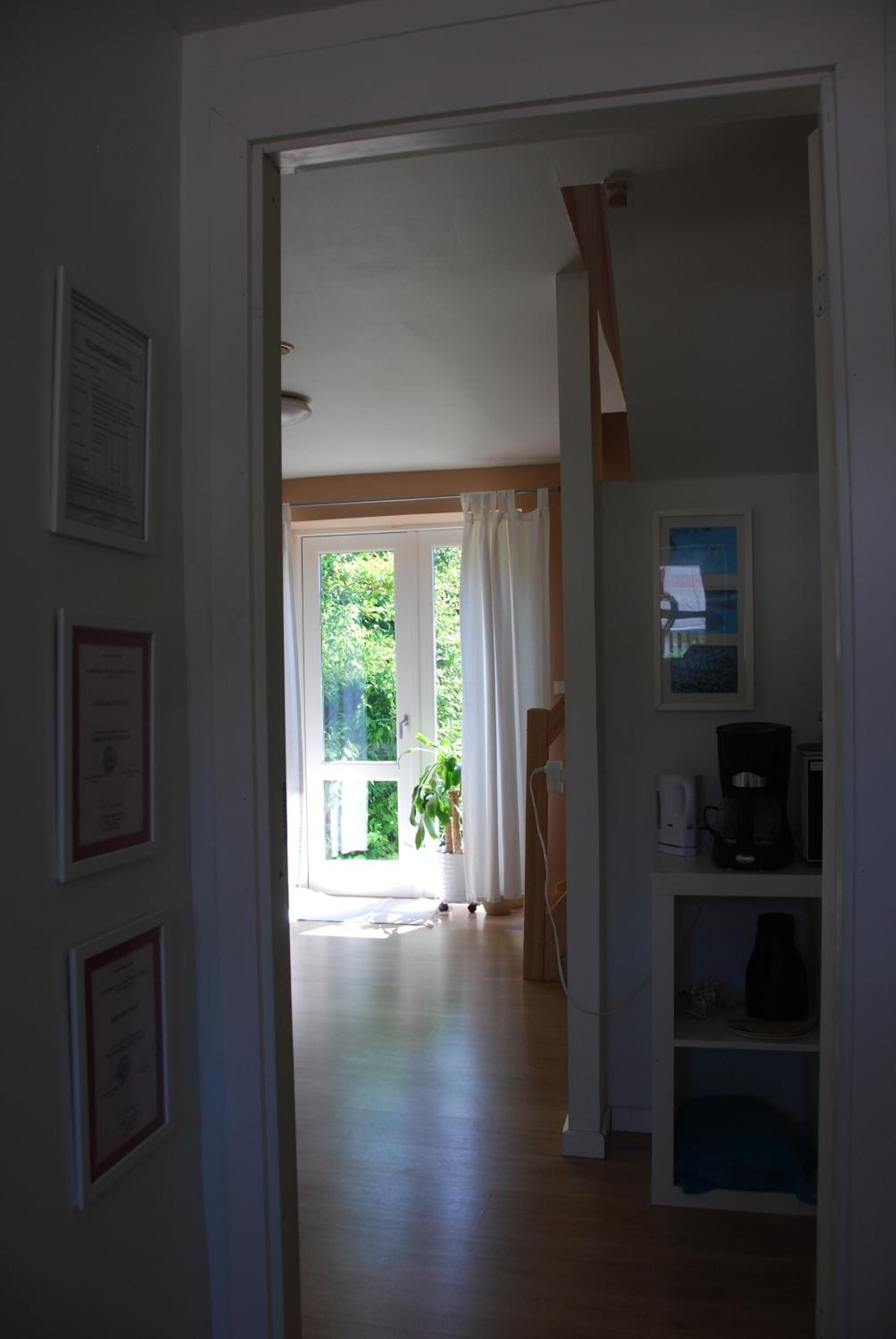 Un pasillo que conduce a una habitación con ventana, una planta y una cafetera.