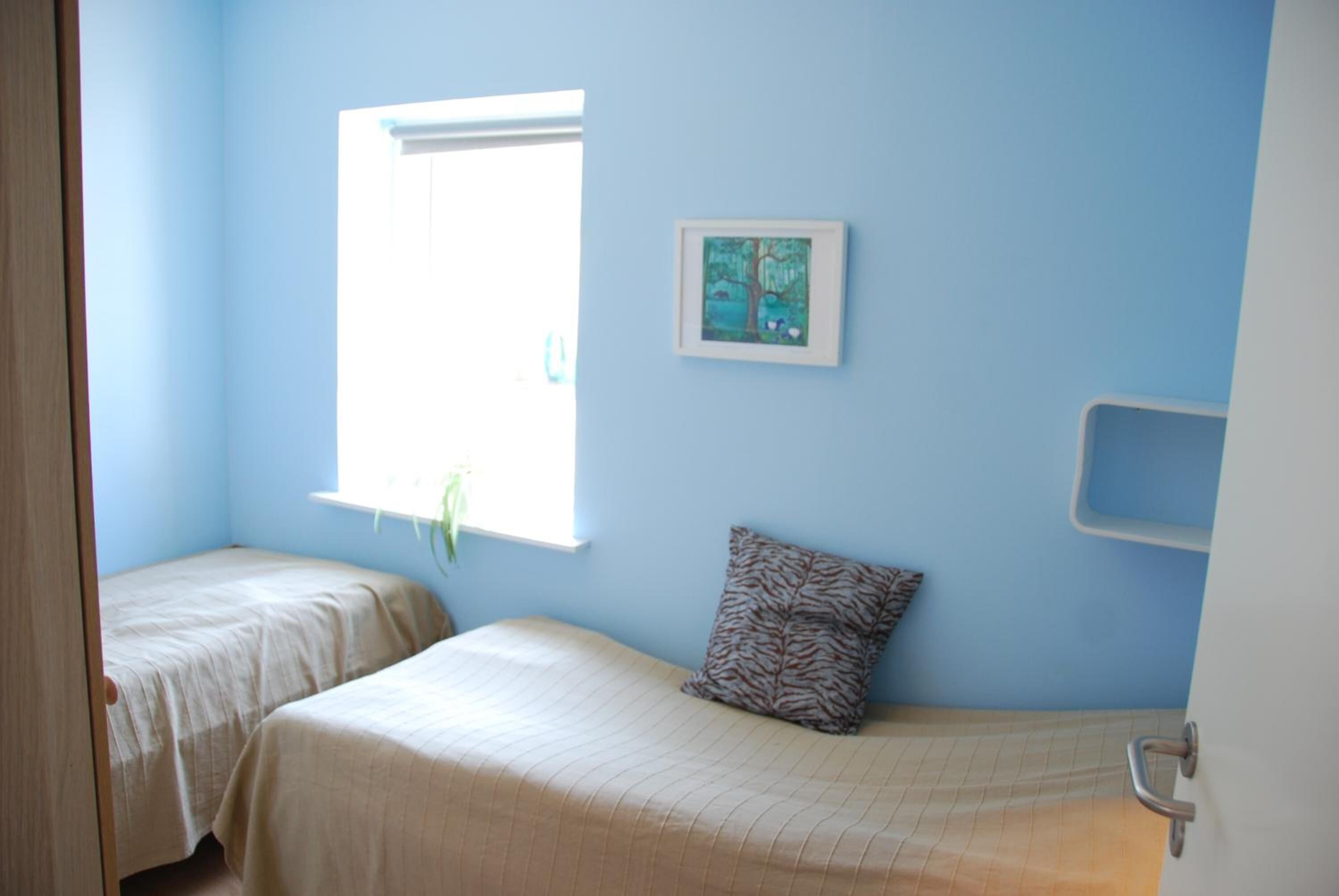 A room with two beds, a window, a framed picture, and a small shelf.