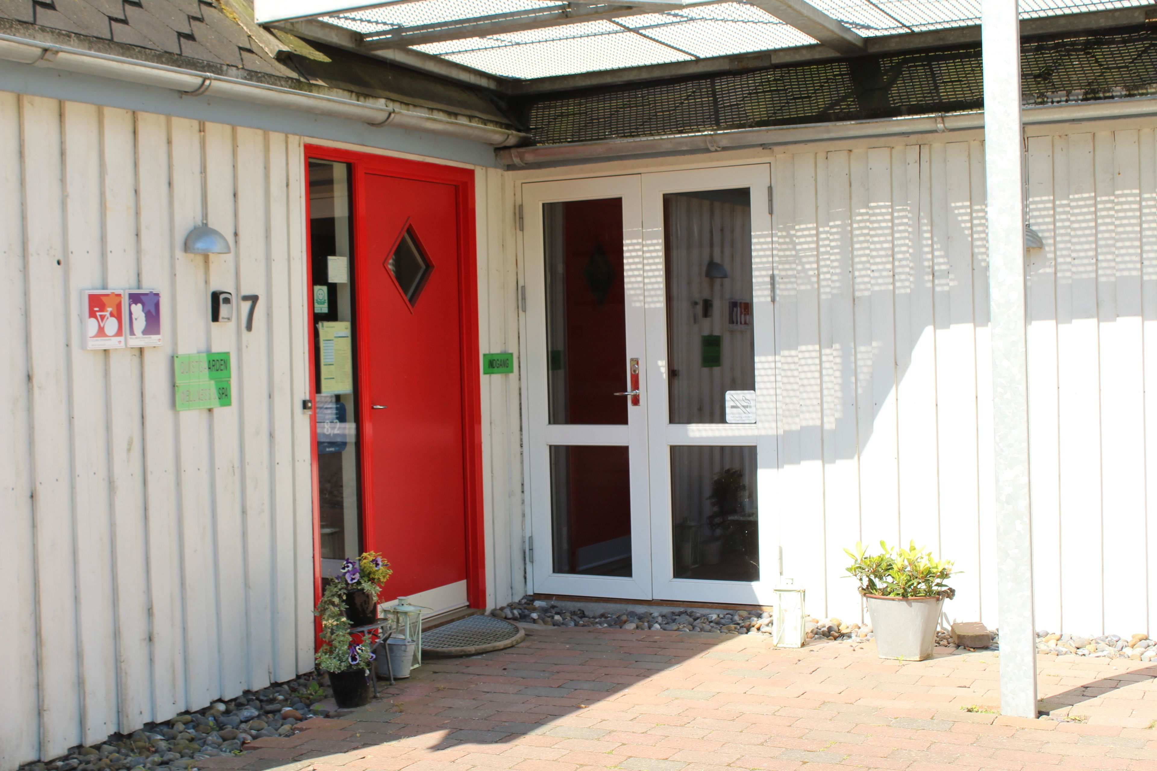 A building entrance with a red door, numbered 7, and a small garden area with potted plants.