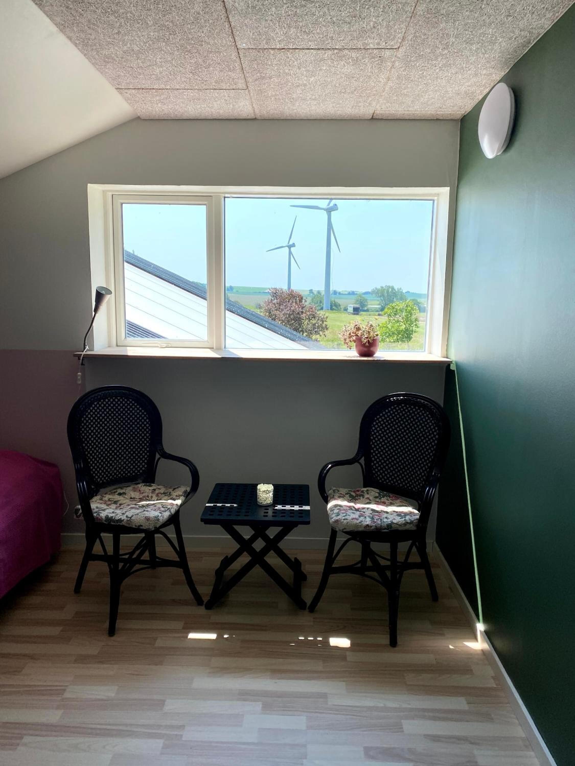 A small room with two chairs, a table, and a window overlooking wind turbines.