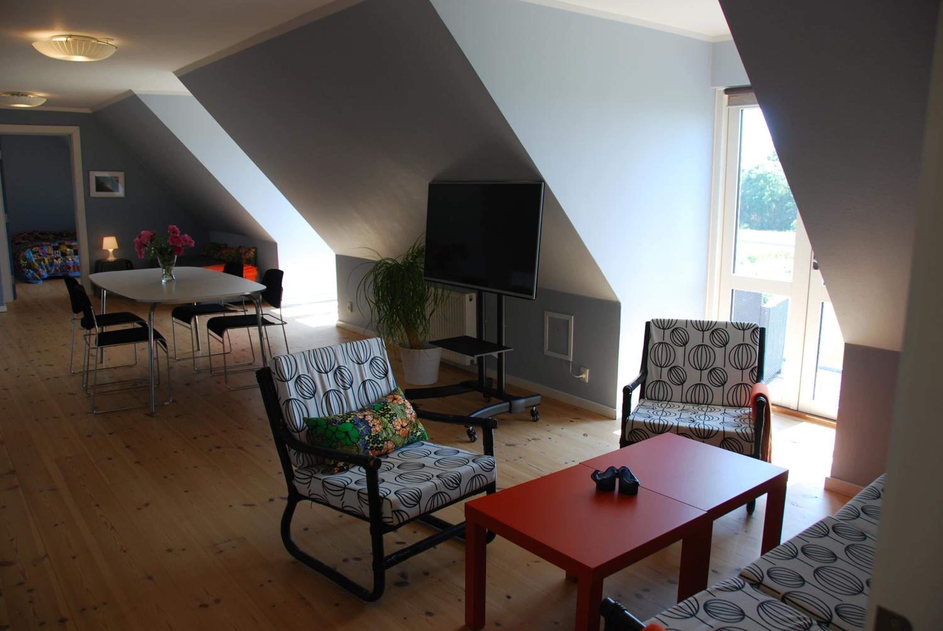 Een modern loft appartement met een eethoek, twee gestreepte fauteuils, een rode tafel en een groot raam.