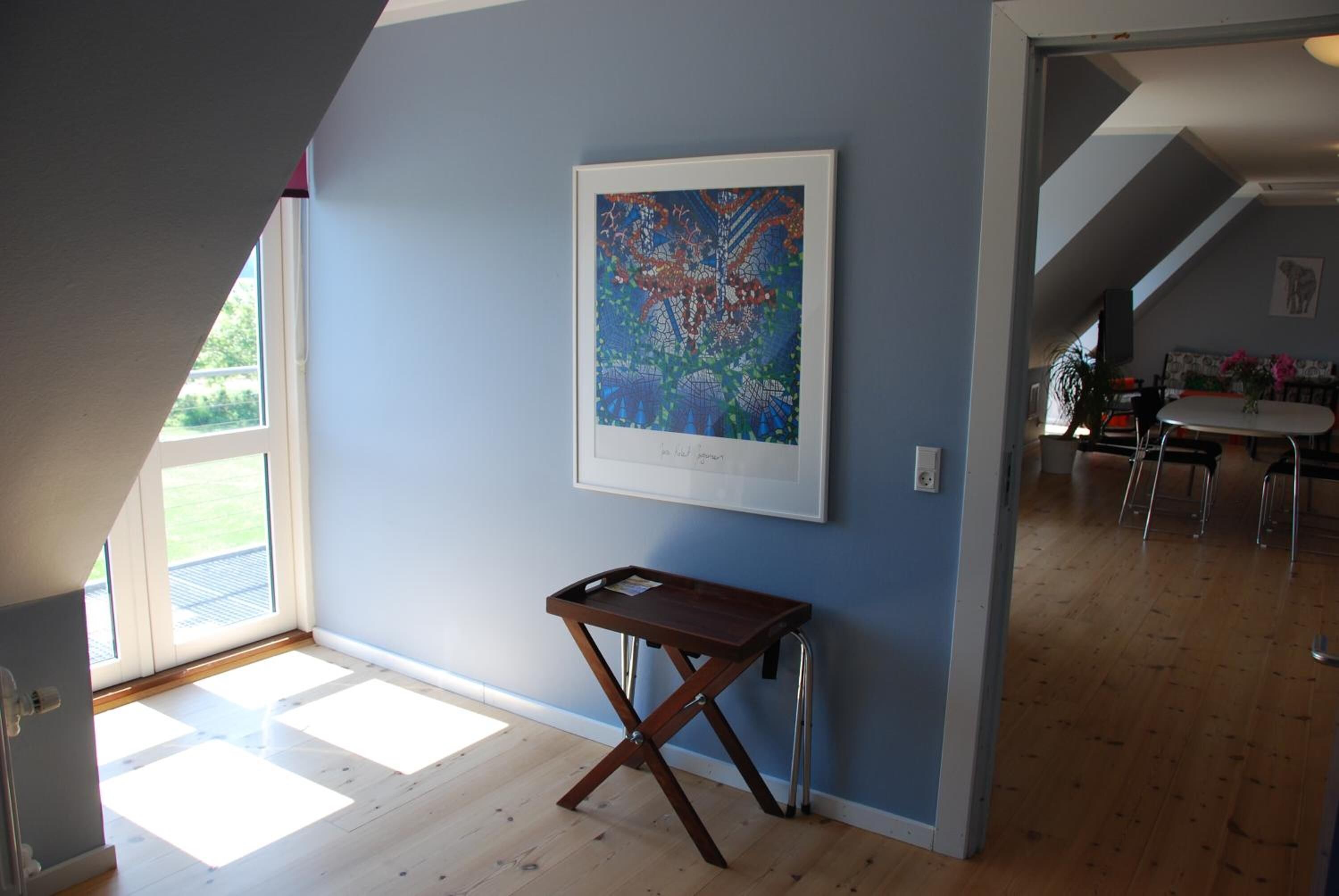 Une pièce avec un plancher en bois, un tableau abstrait encadré accroché au mur et une petite table en bois sur laquelle se trouve un plateau.