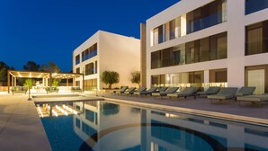Un hotel moderno con piscina, sillas de descanso y una zona de estar cubierta.