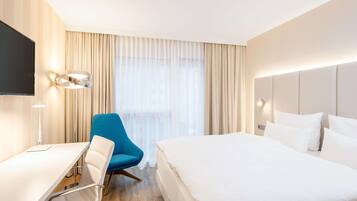 Habitación de hotel con cama, escritorio, silla, televisor y ventana con cortinas.