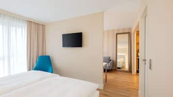 A hotel room with a large bed, a flat-screen TV mounted on the wall, a blue chair, and a view into the hallway.