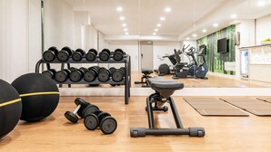 A modern gym with exercise equipment, a mirror, and a wooden floor. - NH Mannheim (Mannheim)