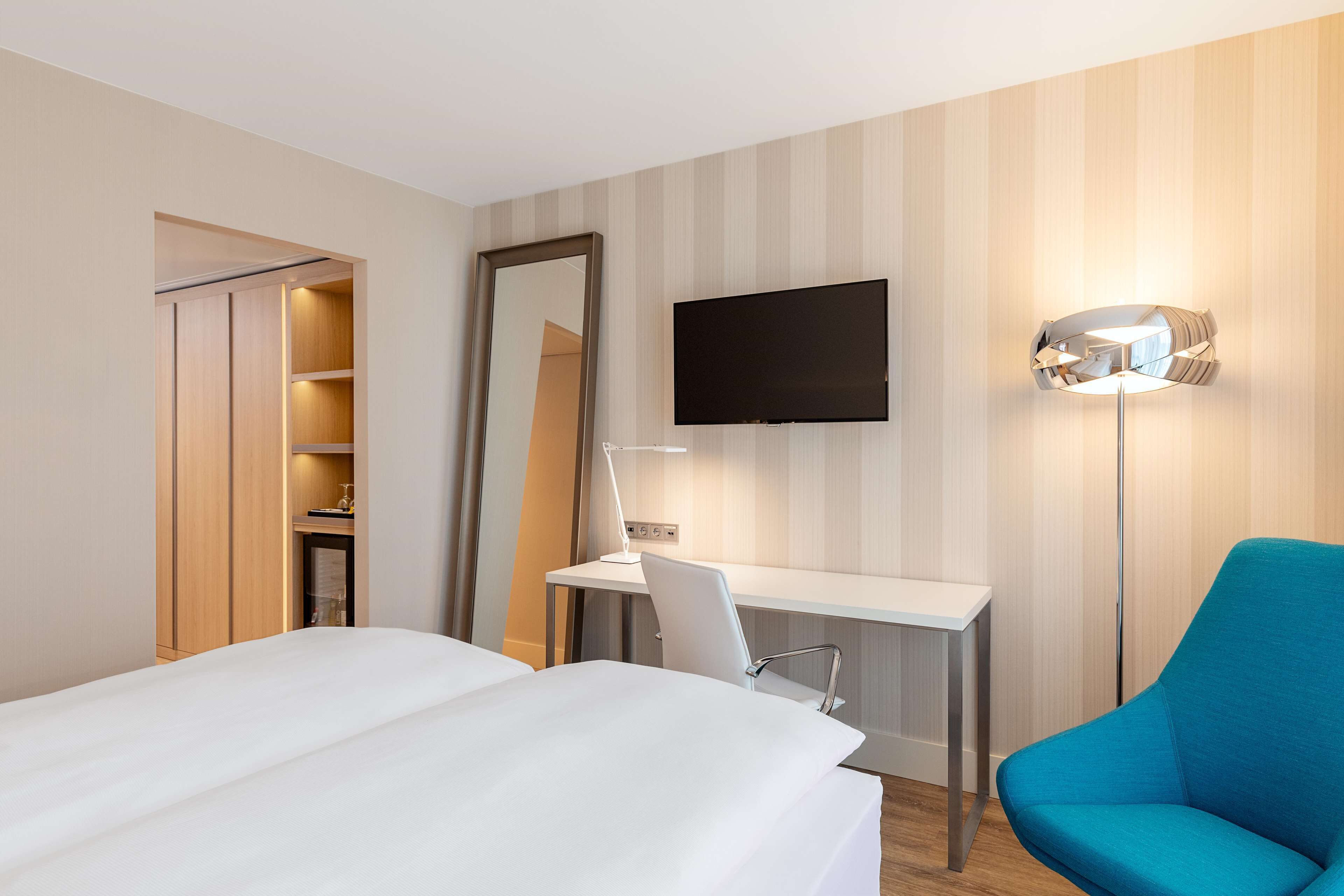 Ein Hotelzimmer mit einem Bett, einem Schreibtisch mit Stuhl, einem Fernseher und einer Stehlampe.