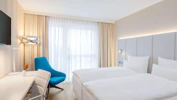 Une chambre d’hôtel avec un lit, un bureau, une chaise, une télévision et une fenêtre avec des rideaux.
