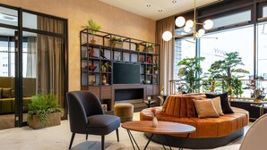 A modern living room with a sofa, chairs, a TV, and a bookshelf. - NH Mannheim (Mannheim)