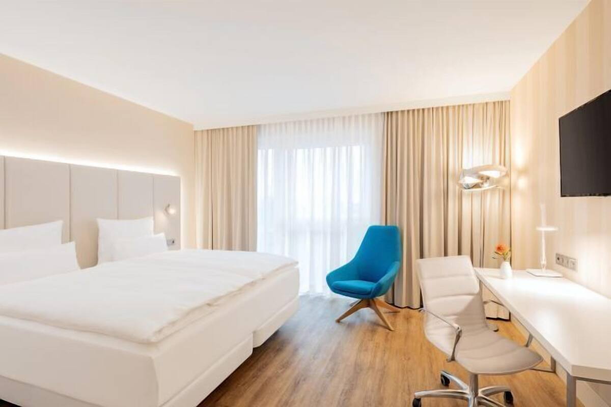 A hotel room with a bed, a desk, a chair, a TV, and a window with curtains.