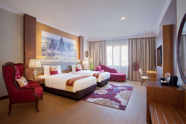 Een hotelkamer met twee bedden, een rode fauteuil, een houten bureau en een groot schilderij aan de muur.