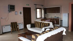 A room with a sofa set, a television, a small table, a chair, a kitchen area with cabinets, and a refrigerator. - Karyon Apartments (Xanthi)